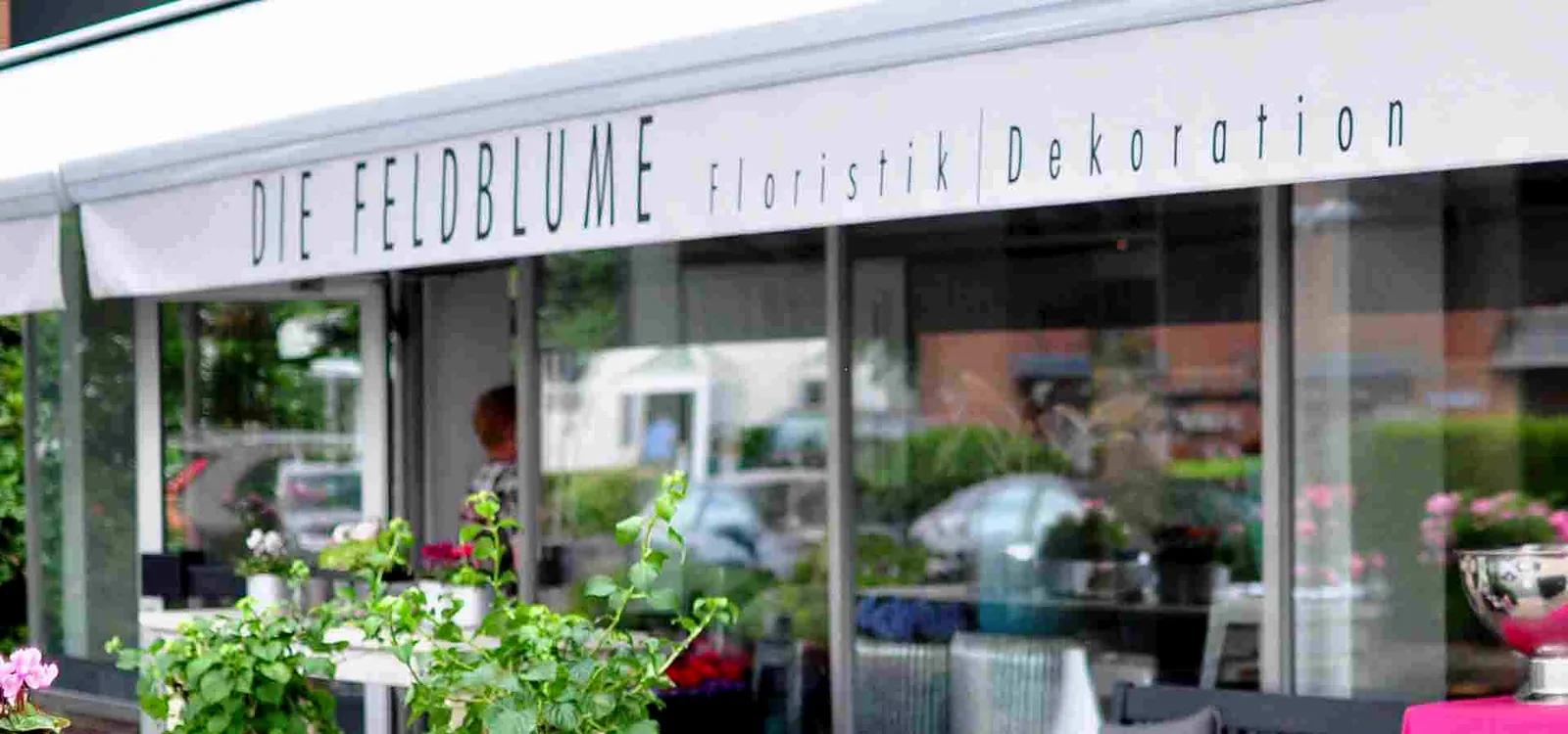 Außenansicht der Feldblume mit Markise und Schriftzug „Die Feldblume — Floristik | Dekoration“