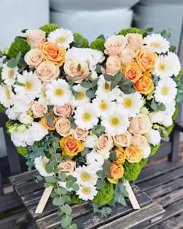 Herz aus weißen Gerbera, lachsfarbenen Rosen und Chrysanthemen auf einer Staffelei