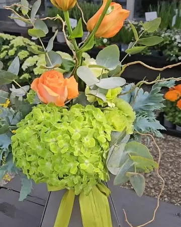 Arrangement aus orangefarbenen Tulpen, grüner Hortensie und Rosen in einem grauen Gefäß